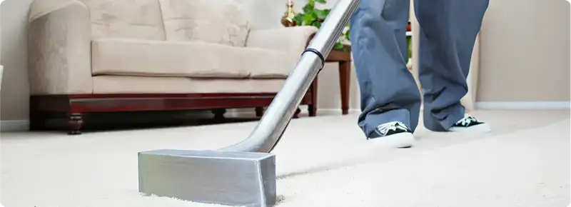 Carpet cleaning technician using a hot-water extraction wand on a light-colored carpet in a living room, Columbia, MO.