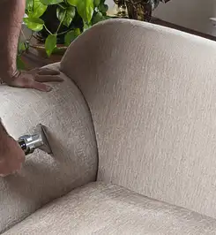 Professional upholstery cleaner deep-cleaning a fabric sofa with a handheld extraction tool and hose Columbia, MO.
