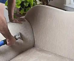 Professional upholstery cleaner deep-cleaning a fabric sofa with a handheld extraction tool and hose in Columbia, MO.